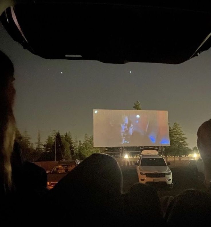 people watching a movie in the back of a car at night with their headlights on