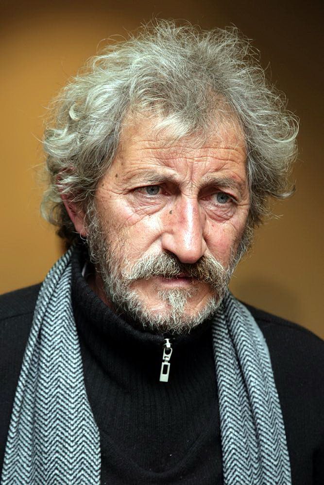 an older man with grey hair wearing a scarf