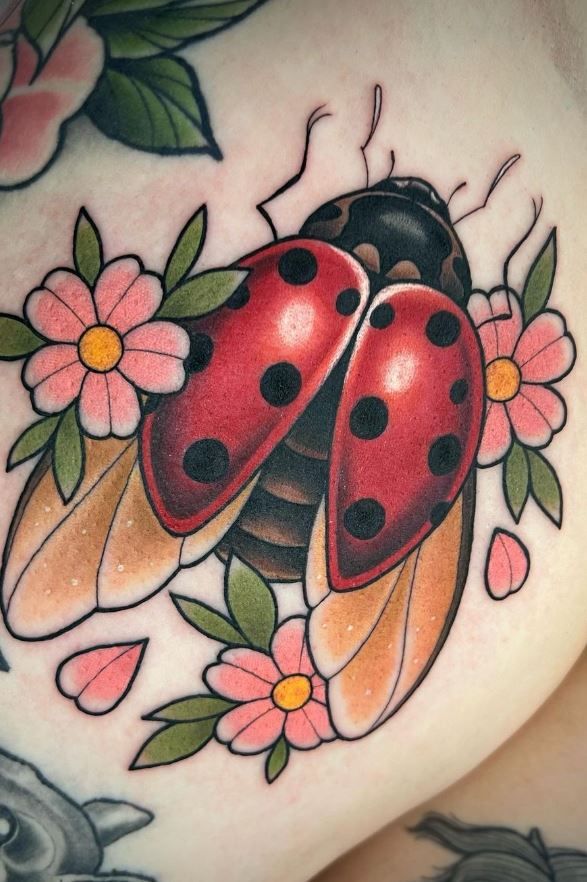 a ladybug tattoo on the side of a woman's stomach with flowers and leaves