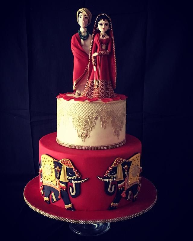 a red and white wedding cake with two figurines on the top, sitting on a stand