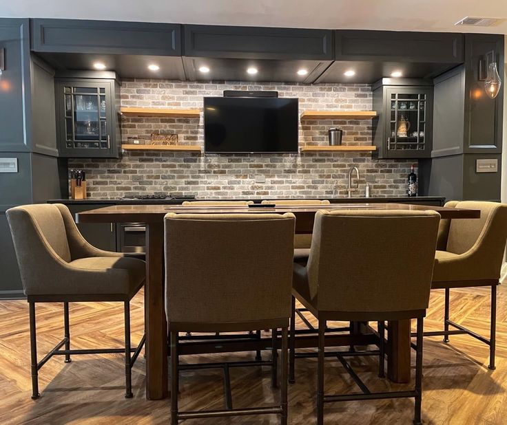 a kitchen with wooden flooring and gray walls has an island table surrounded by brown chairs