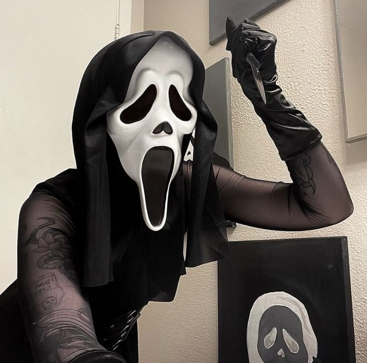 a man dressed in black and white is holding his fist up to the camera while wearing a ghost mask