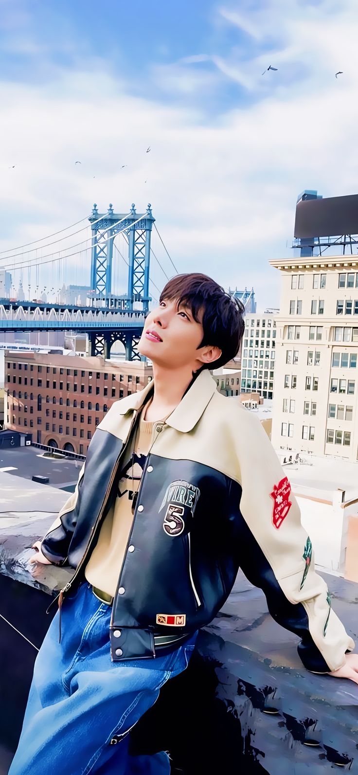 a young man sitting on top of a roof next to a tall building with a bridge in the background