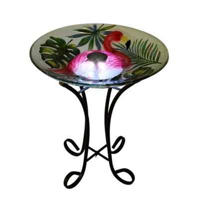 a glass birdbath sitting on top of a metal stand with flowers and leaves painted on it