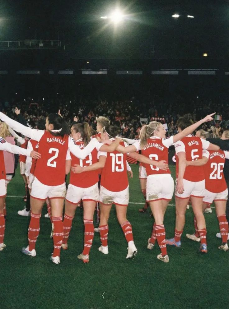 a group of women in red and white uniforms standing on a field with their arms around each other