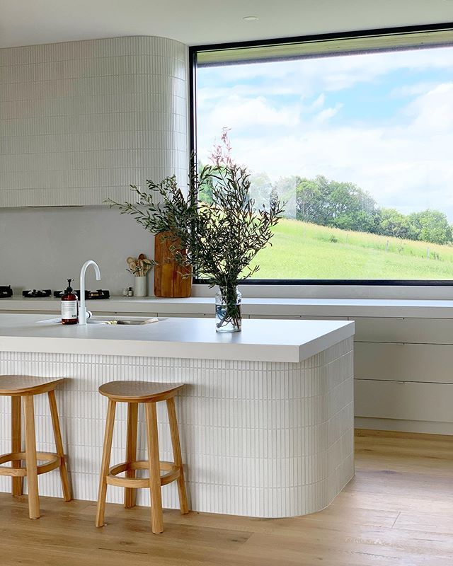 two stools sit in front of an island counter with a large window overlooking a field