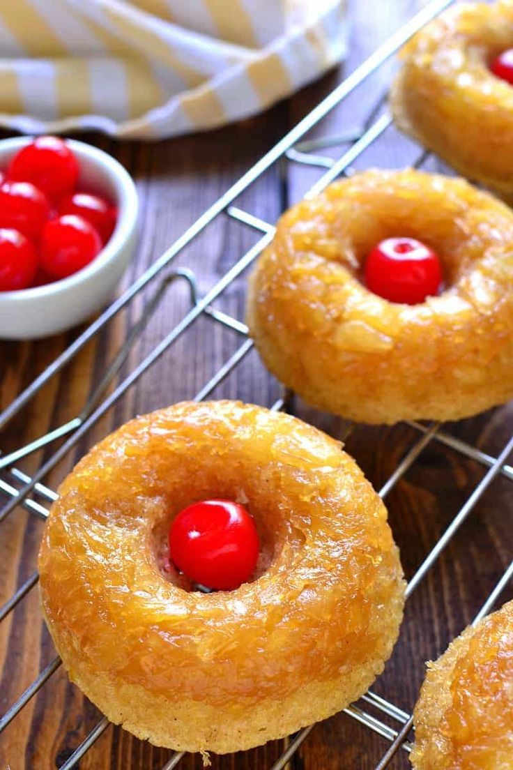 several donuts with cherries are cooling on a wire rack next to small bowls