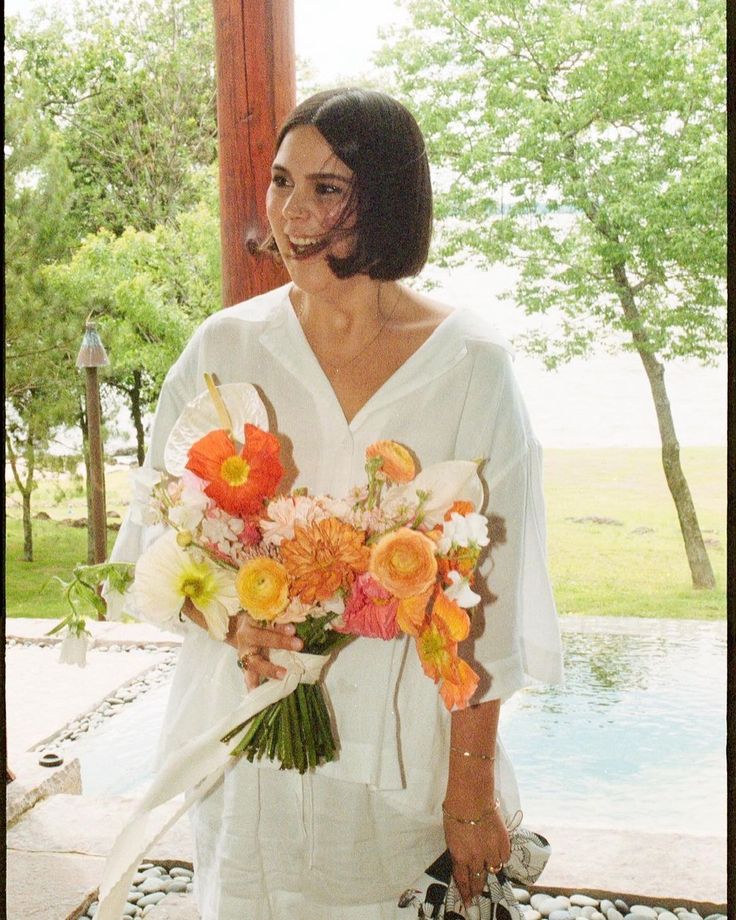 a woman holding a bouquet of flowers in front of her face while standing next to a pool