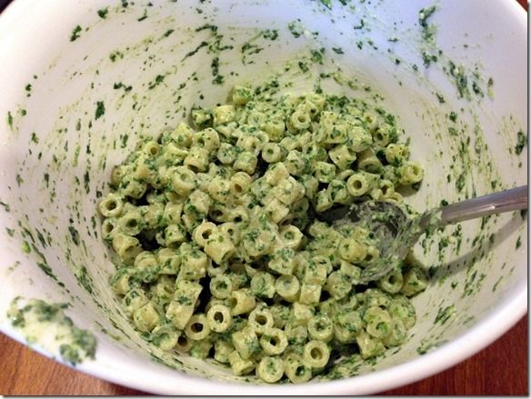 a white bowl filled with green pasta and pesto on top of a wooden table