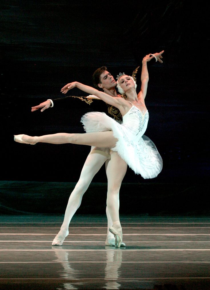 two ballerinas in white tutus and black leotards, one holding the other's leg