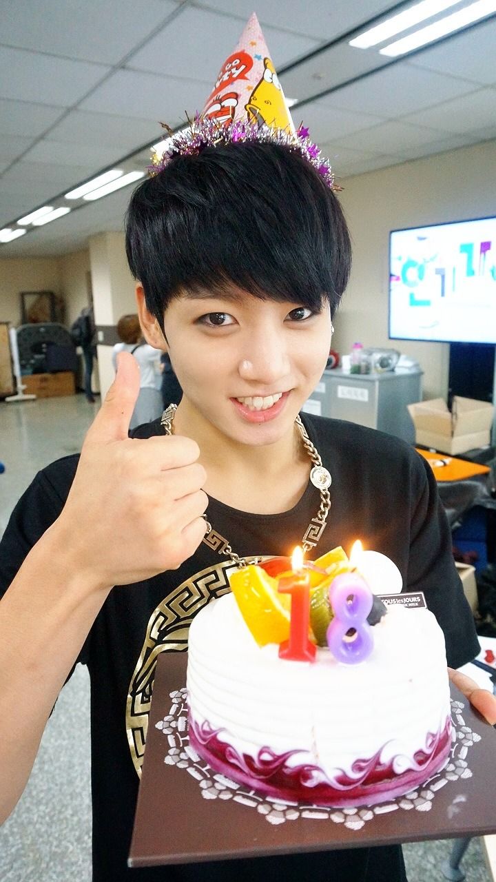 a young man holding a birthday cake with candles on it and giving the thumbs up sign