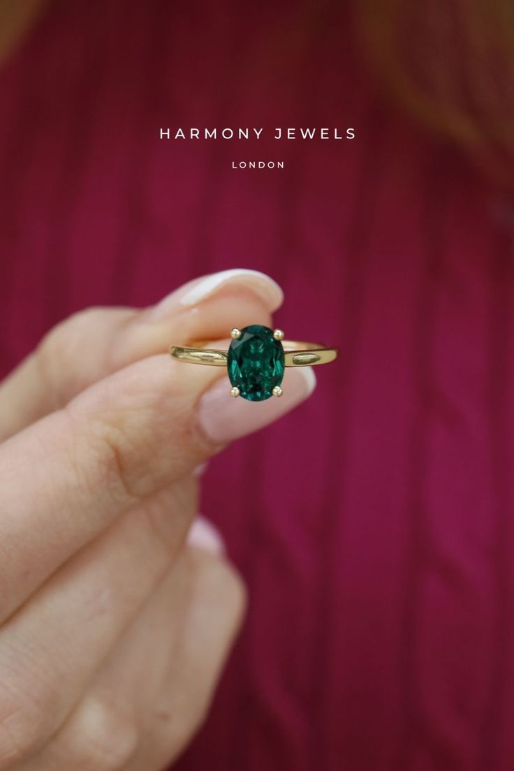 a woman's hand holding a ring with a green gemstone in the middle