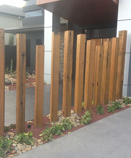 there is a wooden fence in front of the house that has rocks and plants growing on it