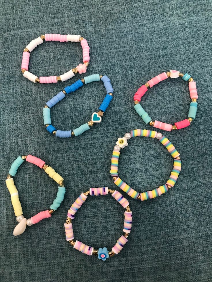 four bracelets with colorful beads and charms on a blue cloth background, including one bead