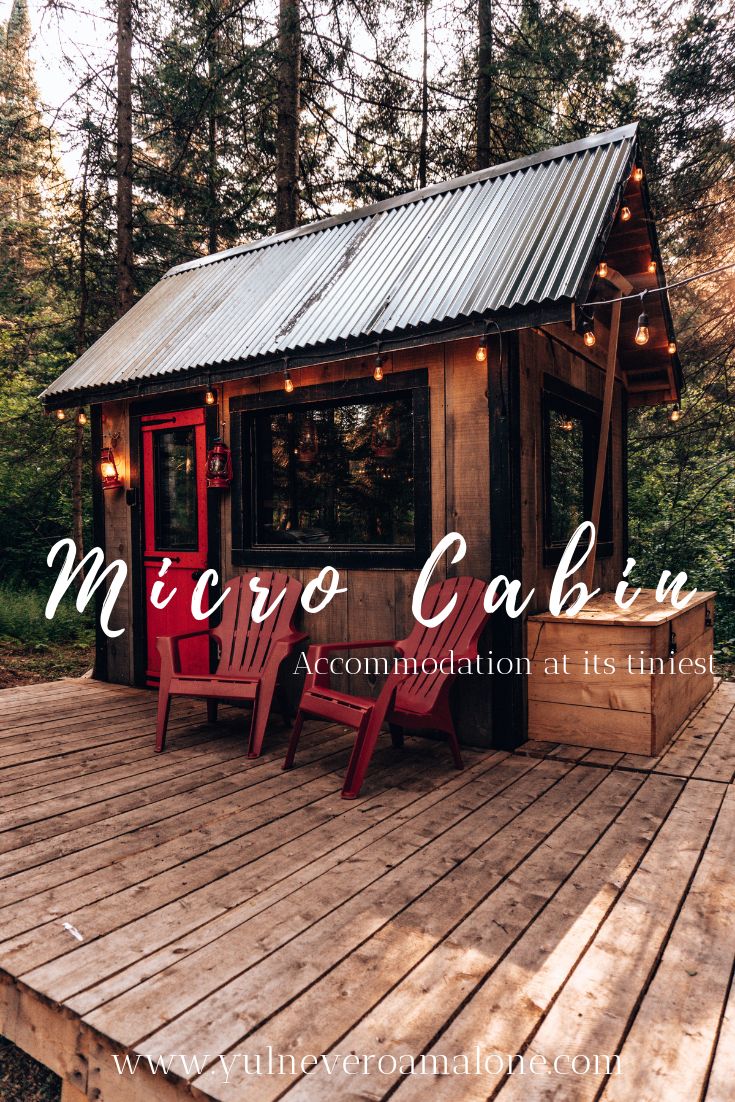 a small cabin sitting on top of a wooden deck with red chairs next to it