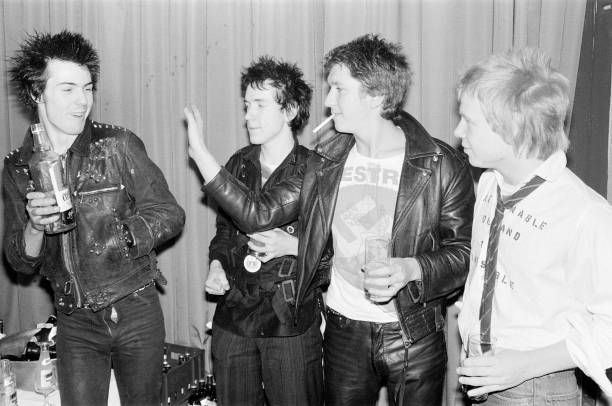 black and white photograph of four young men standing in front of a curtain holding drinks