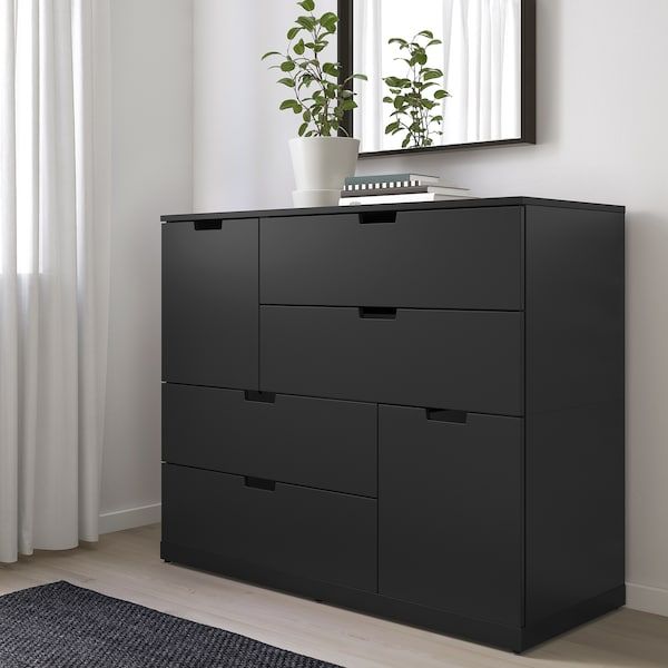 a black dresser with drawers in front of a mirror and potted plant on top