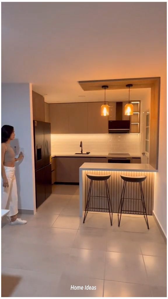 a woman standing in front of a kitchen counter with two stools next to it