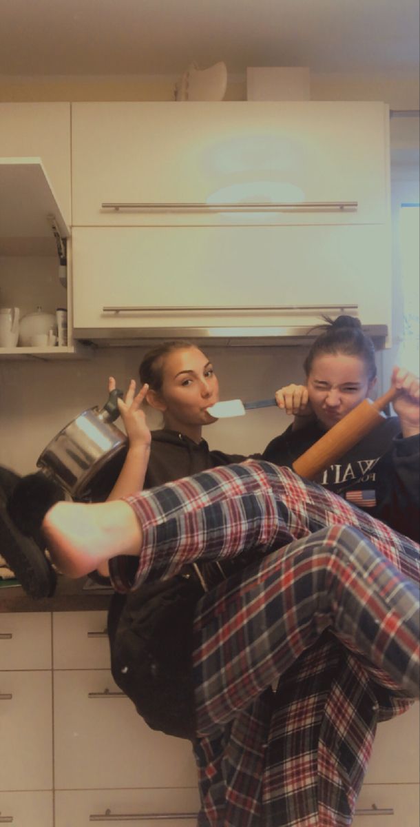 two women are sitting on the kitchen counter and one is holding a baseball bat in her hand