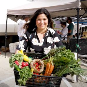 a woman holding a basket full of fresh produce at an outdoor farmer's market