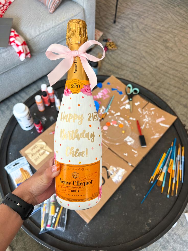 a person holding up a bottle of champagne in front of a table filled with crafting supplies