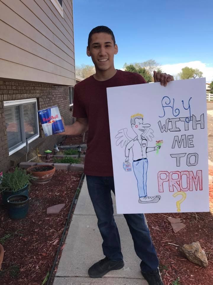 a man holding up a sign that says fly watch me to prom on the sidewalk