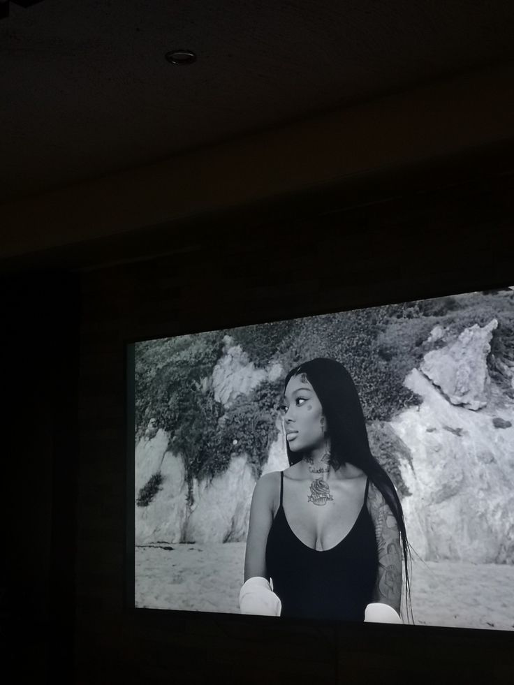 a black and white photo of a woman on a large screen in a dark room