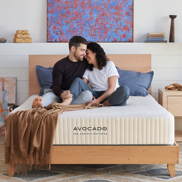 a man and woman sitting on top of a bed next to each other in front of a painting