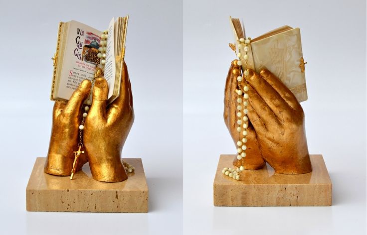 two gold hands holding an open book on top of a wooden block with beads and pearls