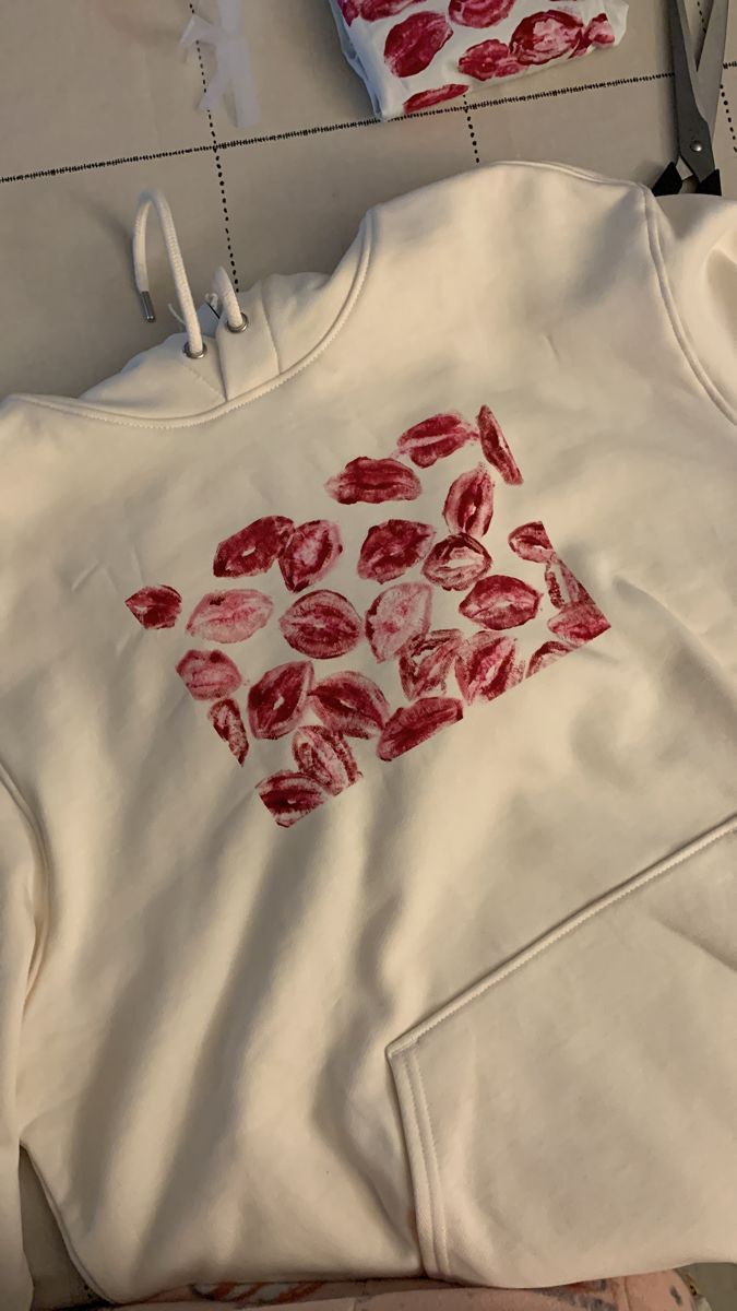 a white sweatshirt with red flowers on it and scissors next to the hoodie that has been cut out