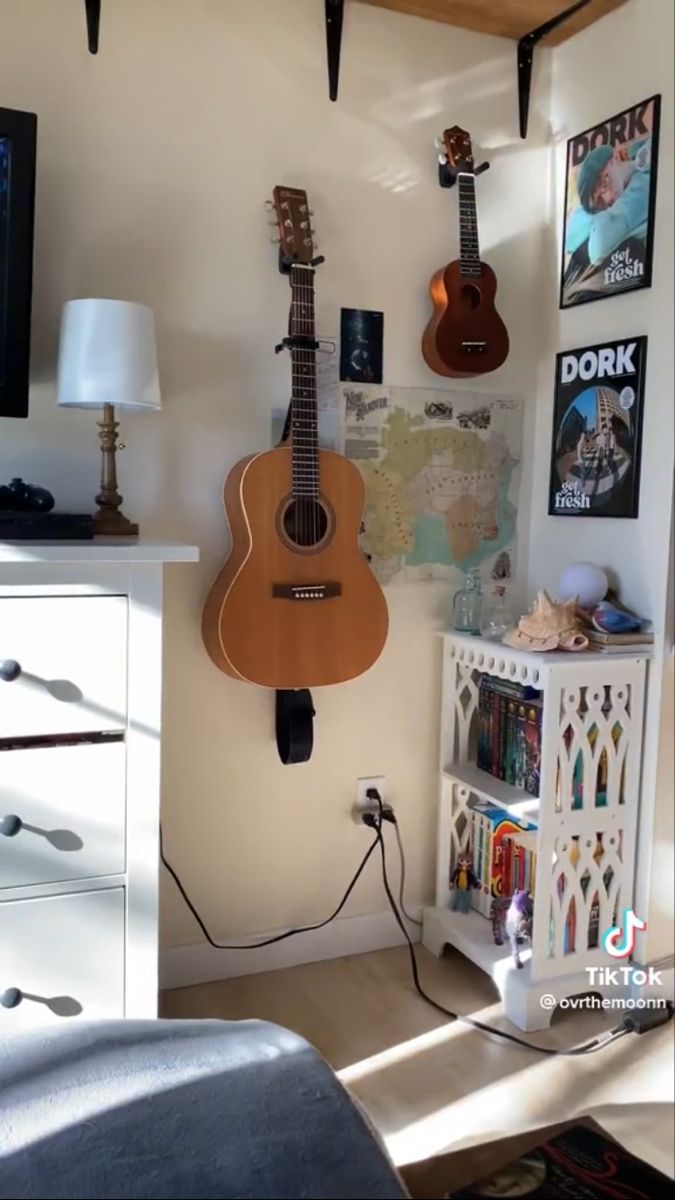 a guitar is hanging on the wall next to a dresser and lamp in a bedroom