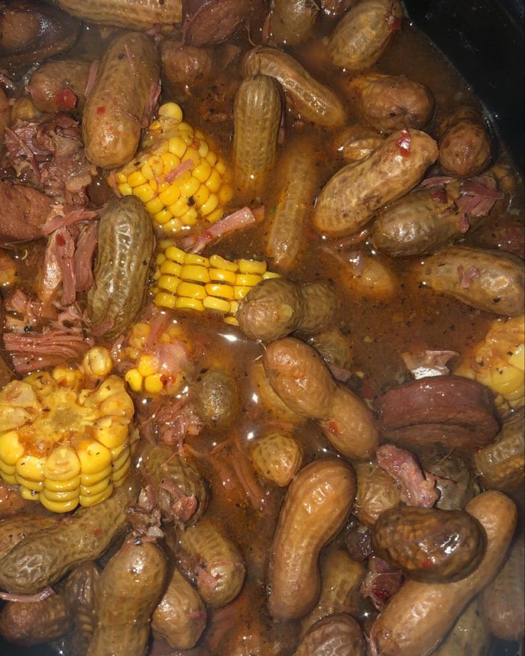 a pot filled with lots of different types of vegetables and meats in liquid next to corn on the cob