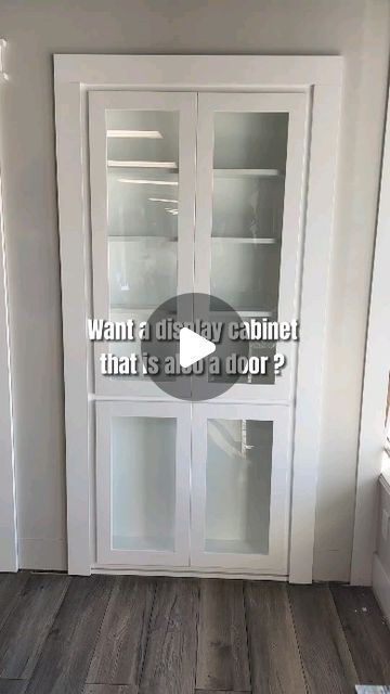 a white cabinet with glass doors in the corner of a room that has wood flooring