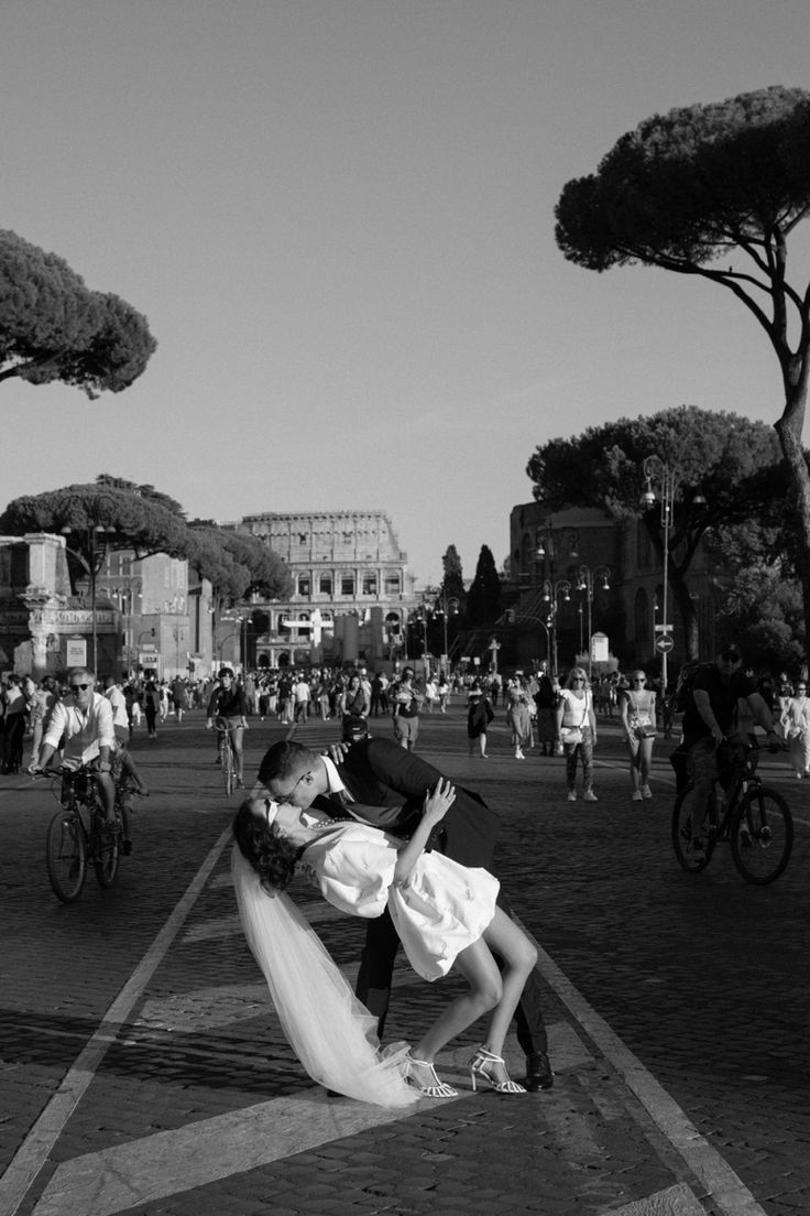 a bride and groom kissing on the street in front of some people with bicycles behind them