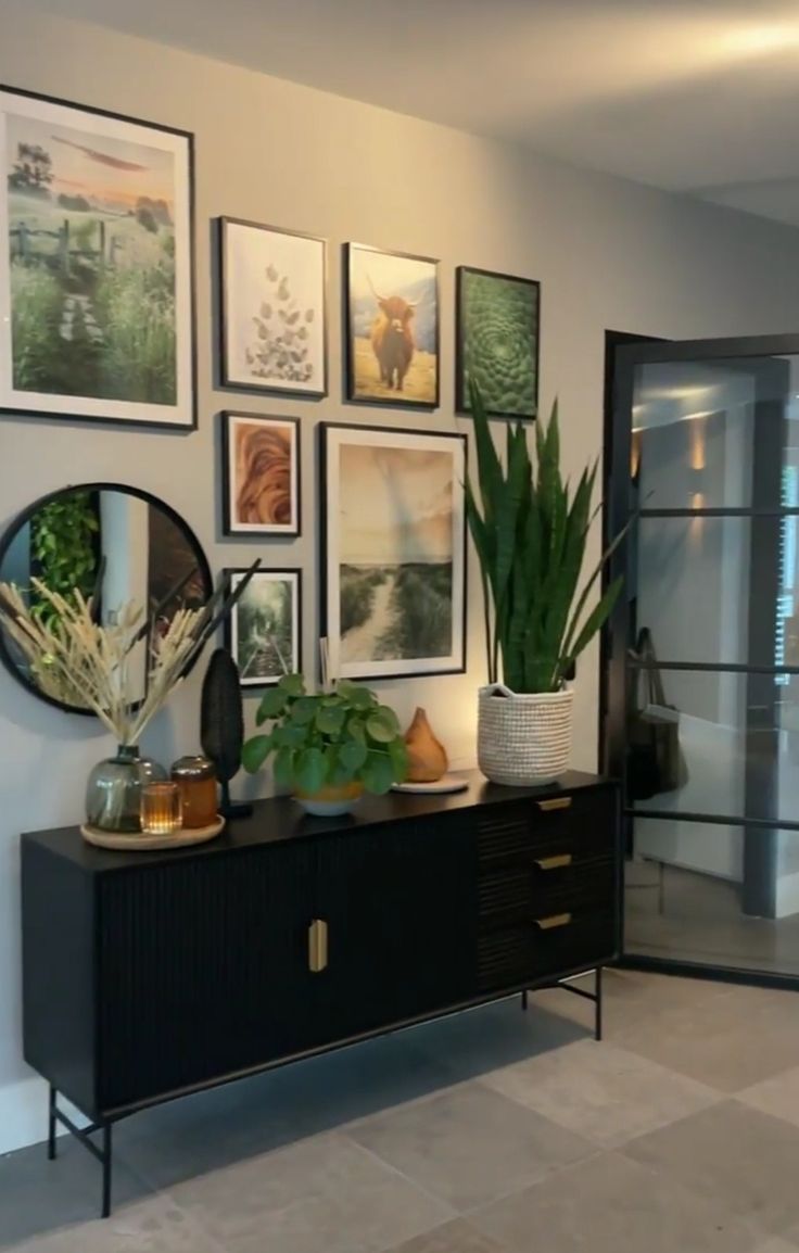 a living room with pictures on the wall and plants in vases next to it