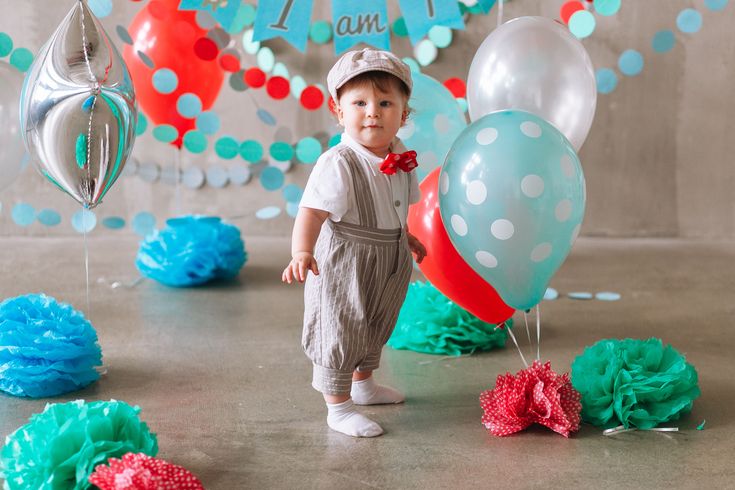 a little boy standing in front of balloons and streamers for his 1st birthday party