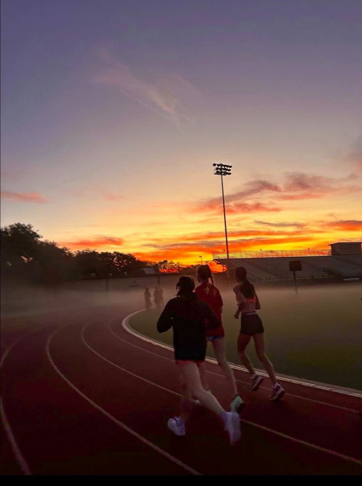 three people running on a track at sunset