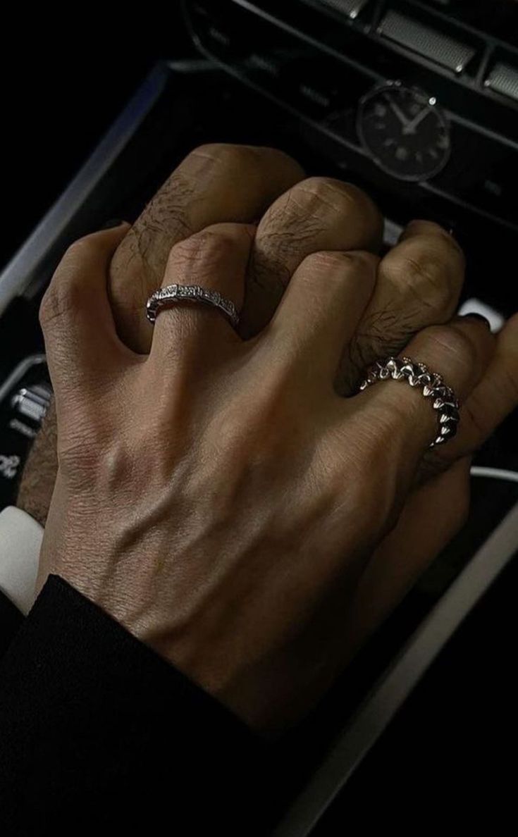 a man's hand with two rings on top of his fingers in front of a watch