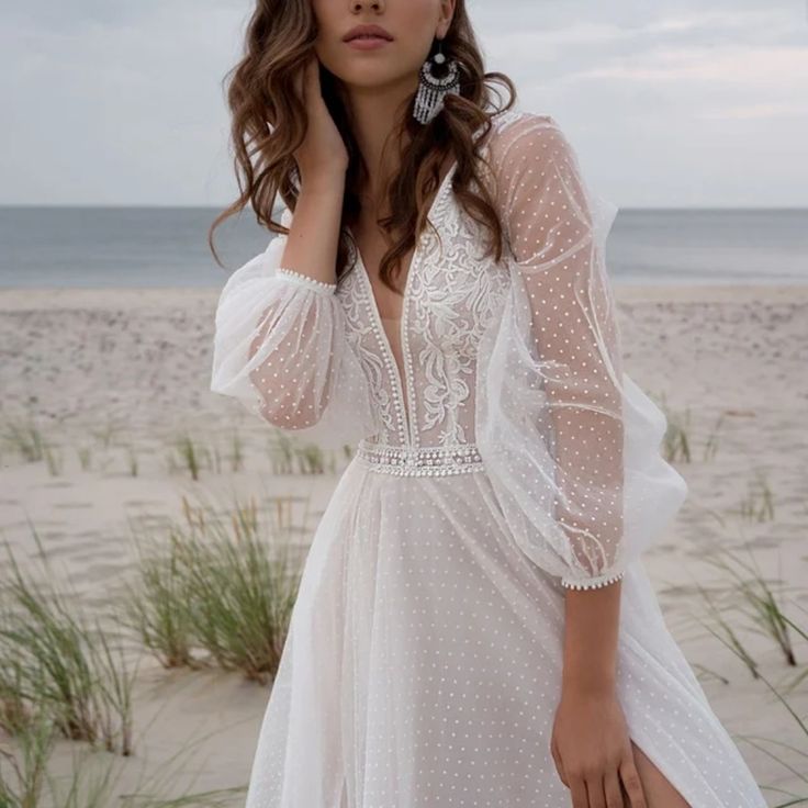 a woman standing on top of a beach next to the ocean wearing a white dress