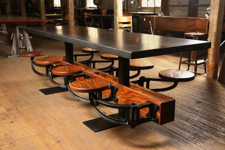 a long table with benches on it in an industrial style restaurant or bar area that has wooden flooring and chairs around the tables