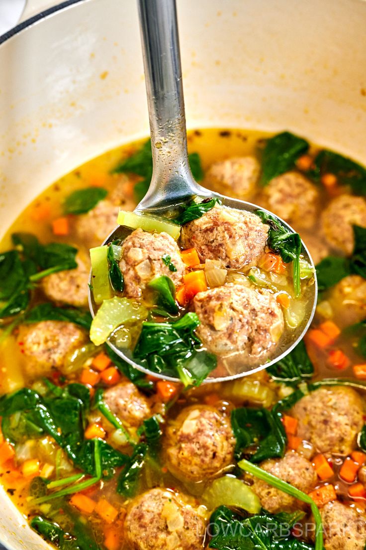 a ladle full of meatball soup with spinach and carrots in it