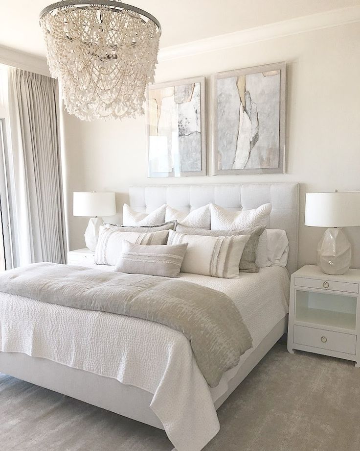 A bright bedroom with a large bed, two white nightstands with lamps, a crystal chandelier, and abstract art above the headboard. The decor is neutral with light tones. Modern White Bedroom, Neutral Bedroom Decor, White Room Decor, John Robshaw, Classy Bedroom, White Bedroom Furniture, Redecorate Bedroom, Bedroom Refresh, Room Makeover Bedroom