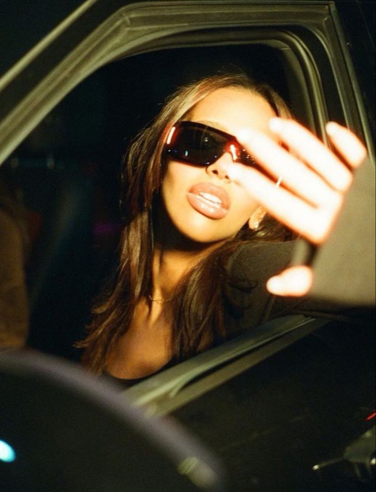 a woman wearing sunglasses sitting in the back seat of a car with her hand up