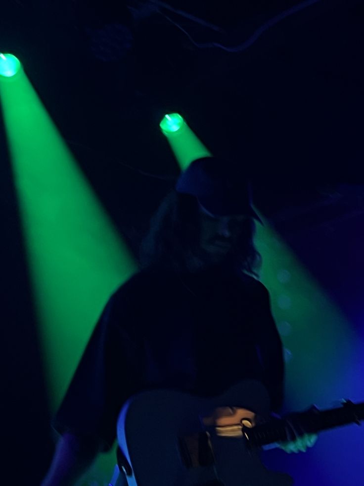 a man holding a guitar in front of green and blue lights