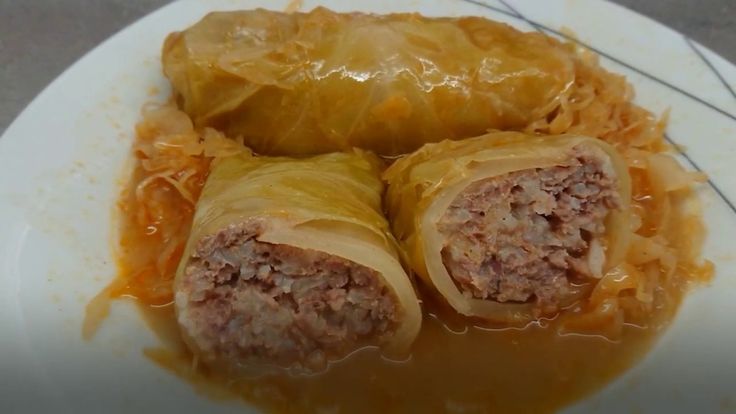 two meat wrapped in cabbage on a white plate with gravy and orange sauce