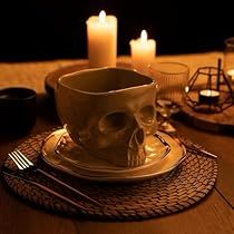 a table topped with a cup and saucer covered in a skull head next to candles