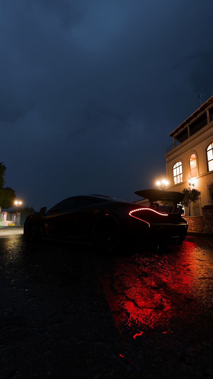 a black sports car parked in front of a building at night with its lights on