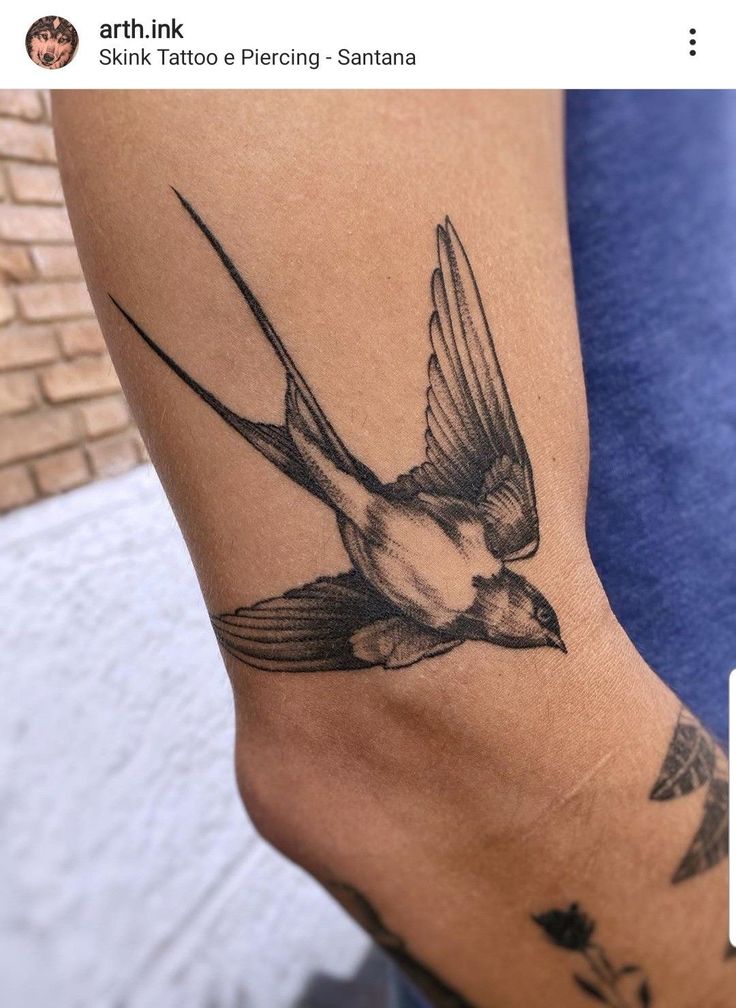 a small bird tattoo on the leg of a person's arm, with one wing extended