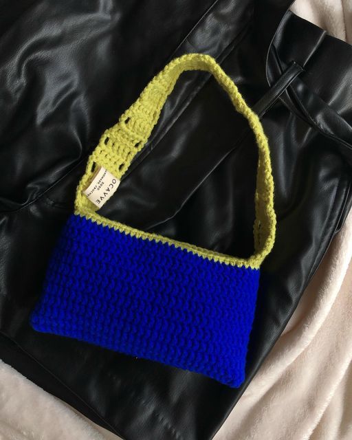 a crocheted blue and yellow purse sitting on top of a black leather bag