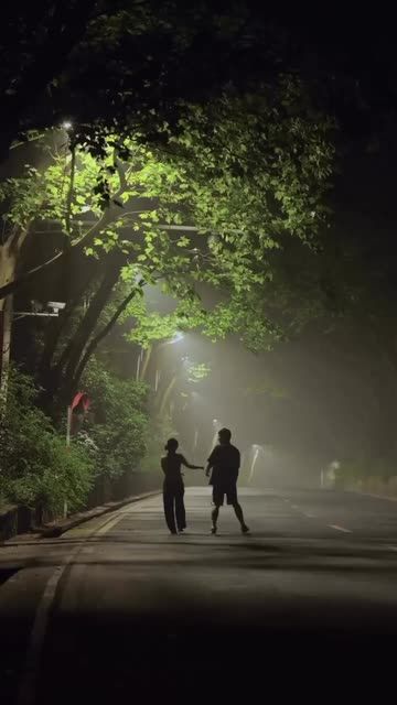 two people are walking down the street at night with their hands in each other's pockets